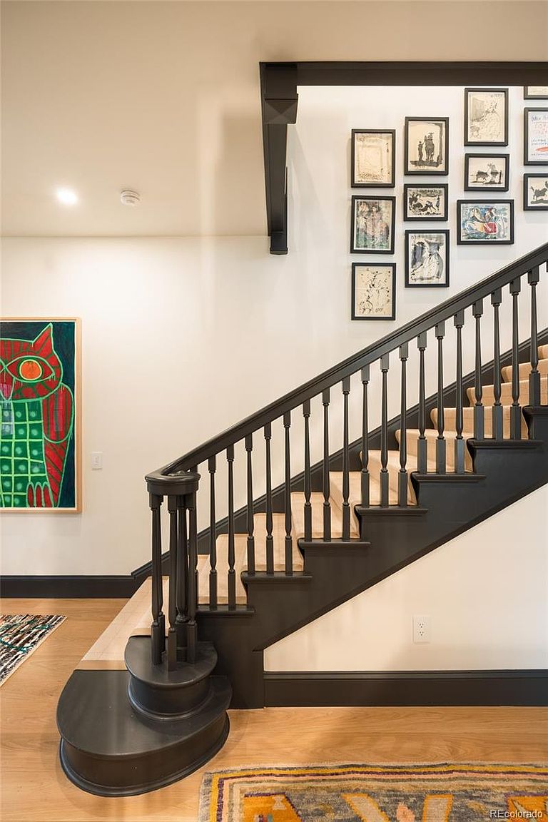 This interior shot showcases a staircase with dark-stained wood steps and railings, complemented by light-colored carpet on the treads. A gallery wall of framed artwork adds character to the white walls, while the hardwood flooring and dark trim create a cohesive and stylish transition space. The staircase features a curved bottom step, adding a touch of elegance.
