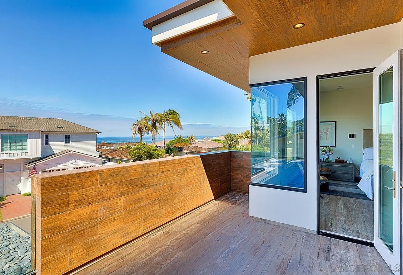 This image showcases a modern balcony with a wood-paneled privacy wall and a view of the ocean. The balcony features a seamless transition to an interior space through large glass windows and doors, offering an indoor-outdoor living experience. The design emphasizes clean lines and natural materials, creating a sophisticated and relaxing atmosphere.