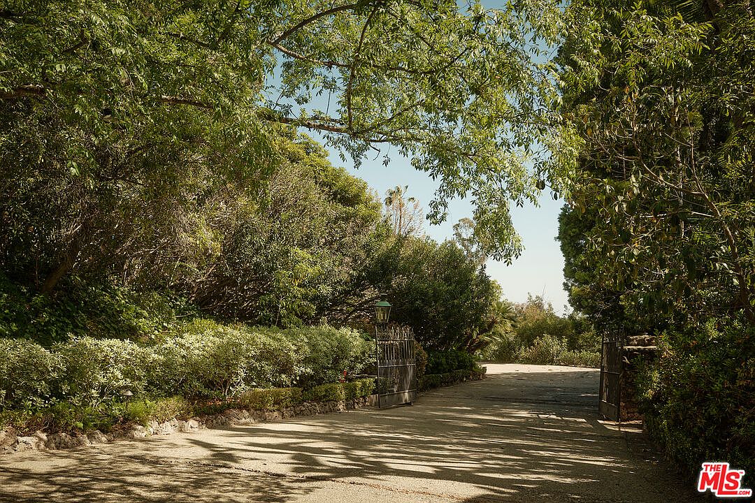 The image showcases a gated entryway leading to a property. Lush greenery and mature trees frame the driveway, creating a sense of privacy and seclusion. The gate itself appears to be made of wrought iron, adding an element of elegance and security to the entrance.