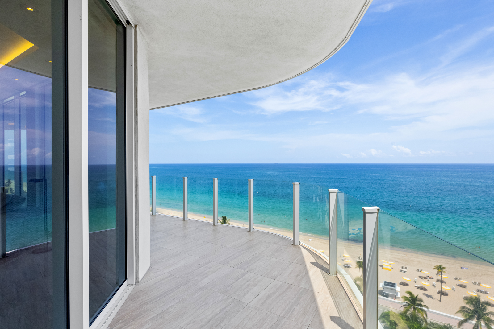 This image showcases a luxurious balcony with stunning ocean views. The balcony features a modern design with glass railings and tiled flooring. The expansive view includes the beach, ocean, and sky, creating a serene and inviting atmosphere, perfect for relaxation and enjoying the coastal scenery.
