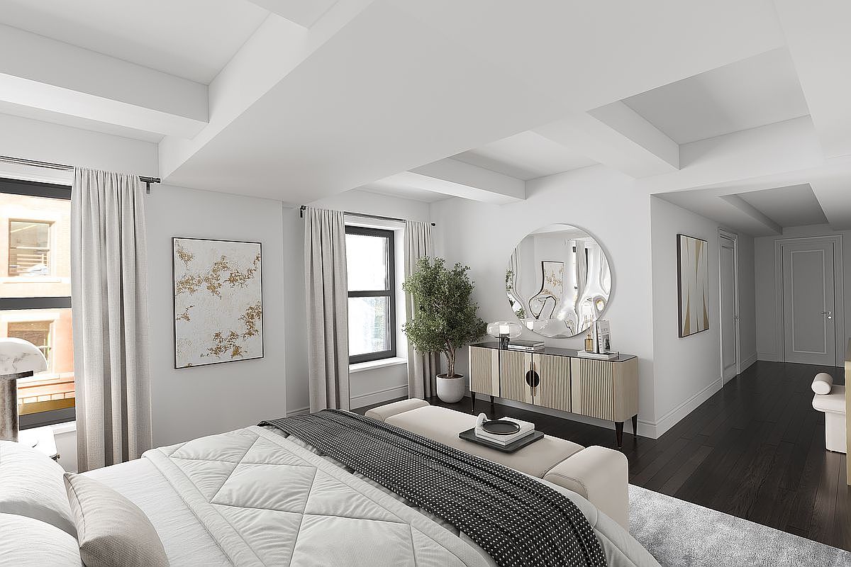 This is a bright and airy primary bedroom featuring a large bed with a white comforter and a gray throw. The room has two large windows with light-colored curtains, a round mirror above a cabinet, and an abstract painting on the wall. The dark wood floors contrast nicely with the white walls and ceiling, creating a modern and inviting space.