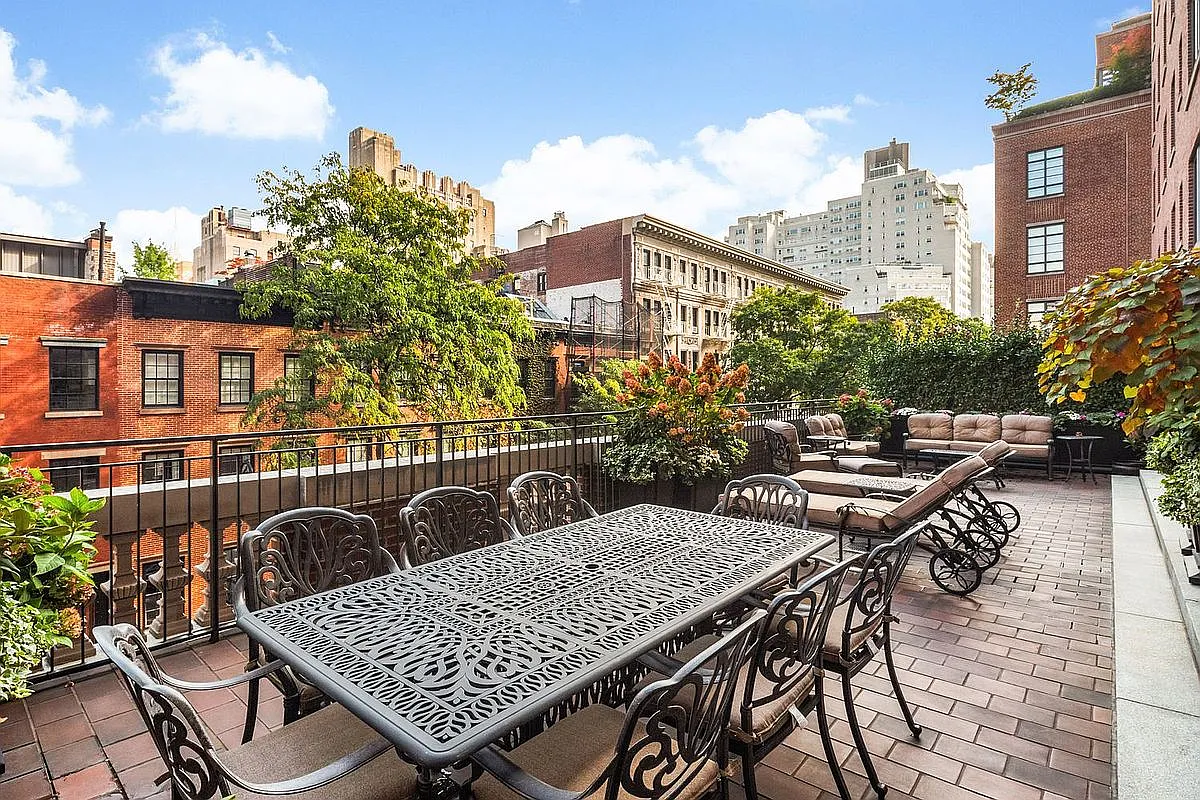 This image showcases a spacious outdoor patio or deck area. It features a large dining table with chairs, as well as lounge furniture, suggesting it's an ideal space for outdoor dining and relaxation. The patio is surrounded by greenery and offers views of the cityscape, creating a luxurious and inviting atmosphere.