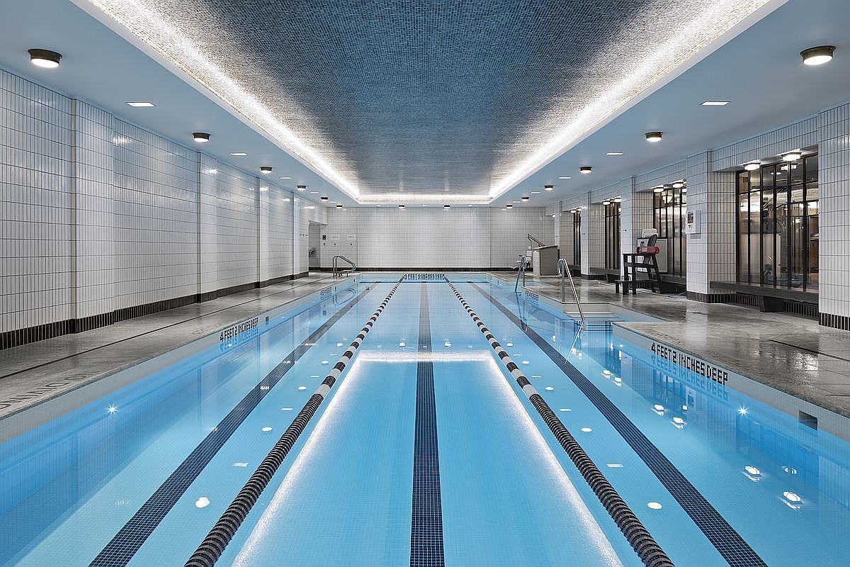 This image showcases a well-lit indoor swimming pool with clear blue water and lane markers. The pool area features tiled walls and a mosaic ceiling, creating a clean and modern aesthetic. A lifeguard chair is visible, suggesting a safe and well-maintained environment.