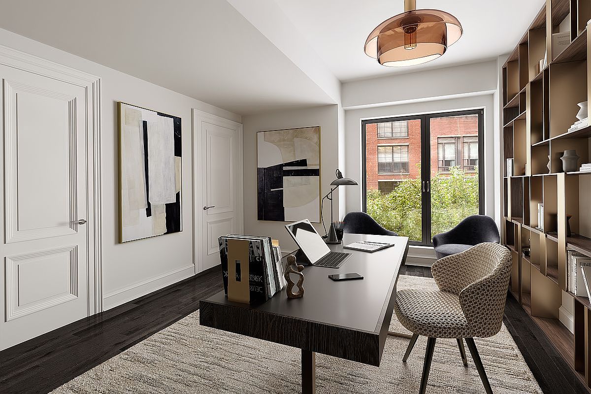 This is an interior shot of a modern office space featuring a dark wood desk with a laptop, books, and decorative items. The room is well-lit with a unique ceiling light fixture and natural light streaming through a large window, complemented by a built-in bookshelf on the right and abstract art pieces on the walls. The overall impression is a sophisticated and functional workspace.