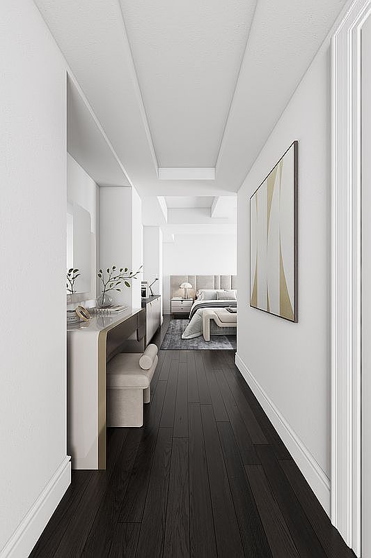 This interior shot showcases a modern hallway leading into a bedroom. The hallway features dark hardwood floors, white walls, and a contemporary art piece. A vanity area with a stool is visible on the left, adding a touch of luxury and functionality to the space.