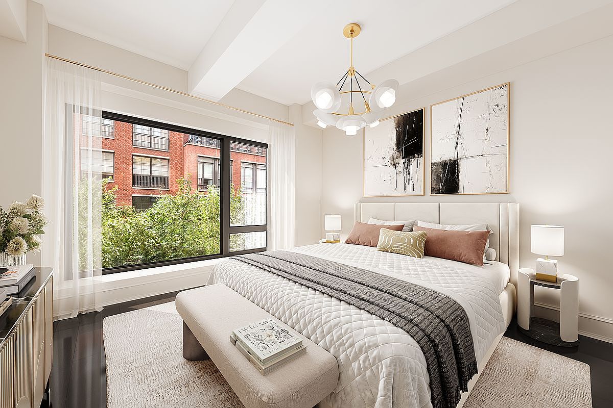 This is a bright and airy primary bedroom featuring a large window with views of greenery and a neighboring building. The room is decorated in neutral tones with a white upholstered bed, abstract art above the headboard, and a modern chandelier. A bench sits at the foot of the bed, and the overall impression is one of calm and sophistication.