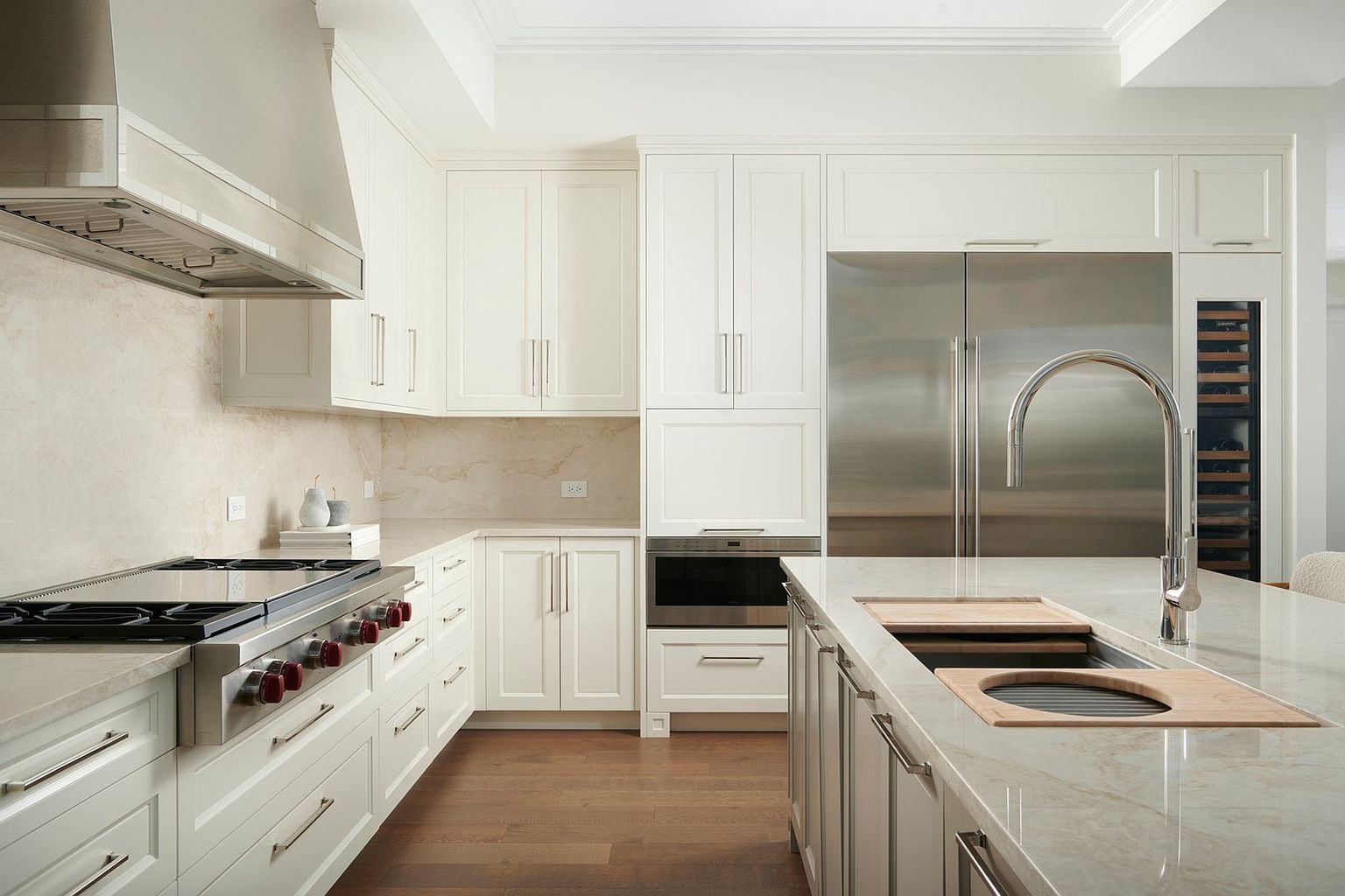 This sophisticated, high-end kitchen features crisp white cabinetry, premium stainless steel appliances, and elegant stone countertops. The central island includes an integrated sink and wooden cutting board inserts, while the warm hardwood flooring provides a beautiful contrast to the bright, clean aesthetic. The perspective is a straight-on, eye-level shot that highlights the seamless flow and professional-grade design of this luxury culinary space.