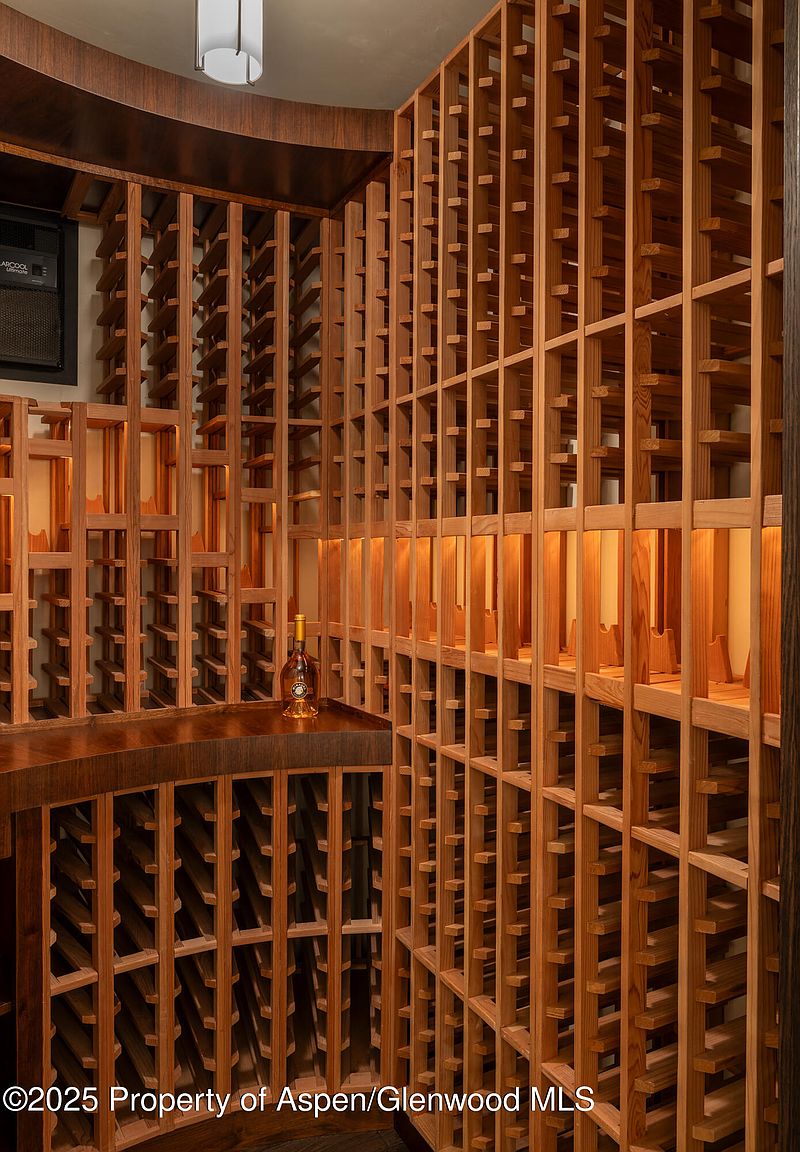 This image showcases a well-organized wine cellar with custom wooden racking. The racks are filled with empty spaces, suggesting ample storage capacity. A single bottle of wine sits on a wooden counter, adding a touch of elegance. The lighting is warm and inviting, highlighting the wood's natural tones and creating a sophisticated atmosphere.