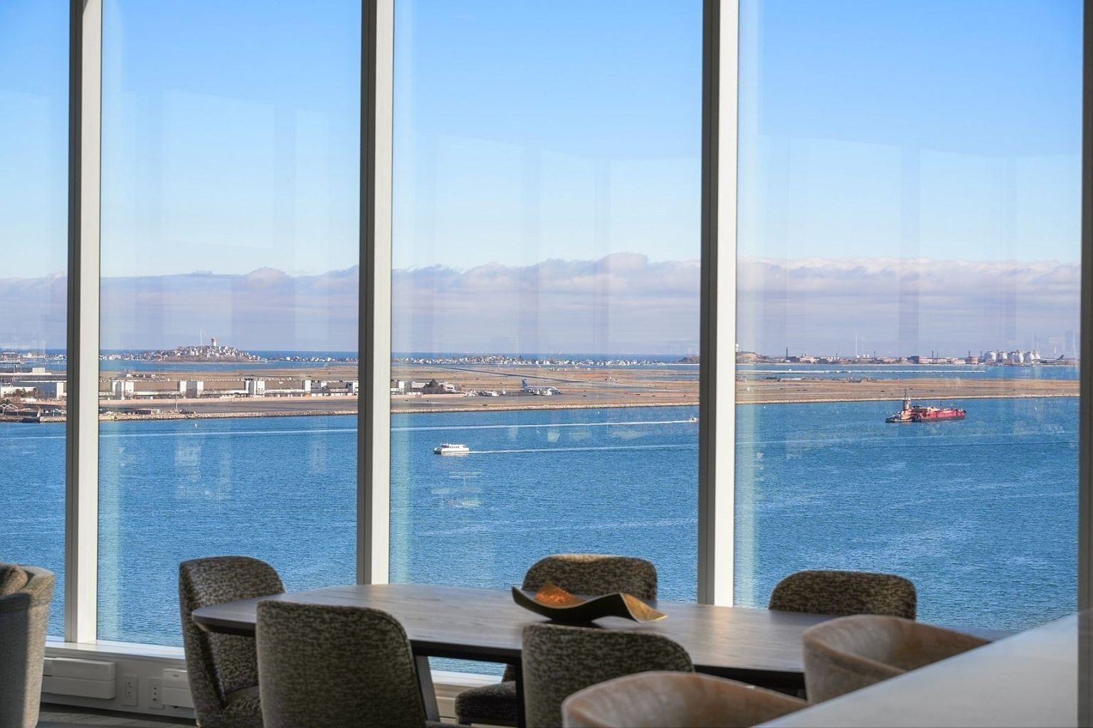 This interior shot showcases a dining room with a stunning panoramic view of the ocean and cityscape through large windows. A modern dining table with chairs is centered in the room, suggesting a space for elegant meals with a breathtaking backdrop. The room exudes a sense of luxury and sophistication, highlighting the property's prime location and upscale design.