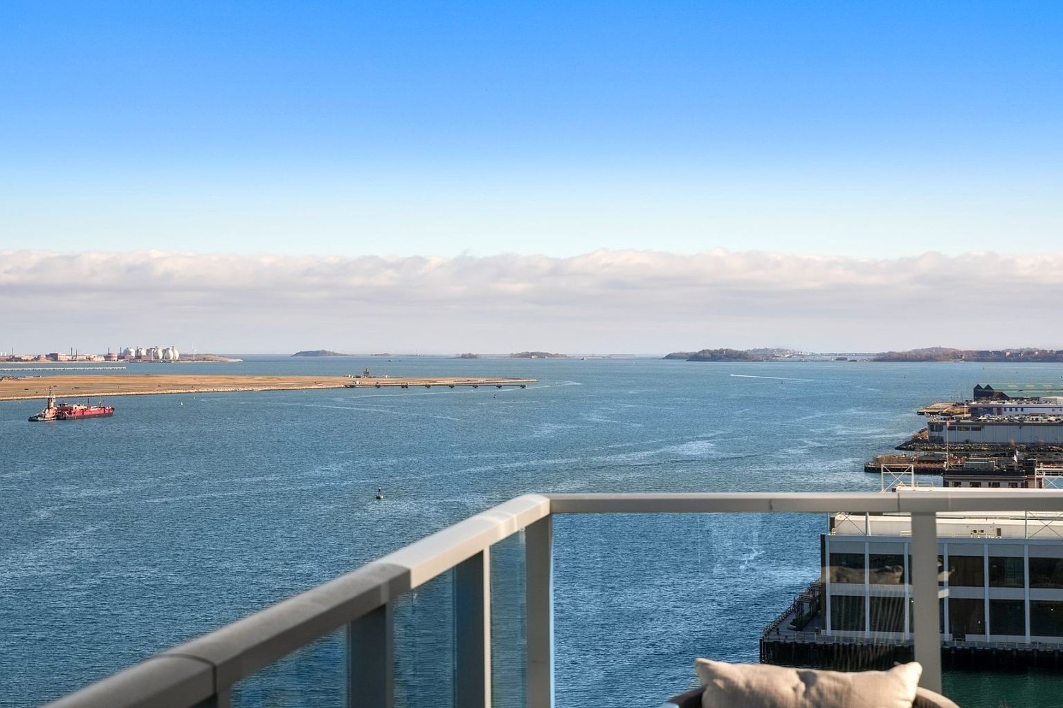 This image showcases a stunning waterfront view from a modern balcony. The balcony features a glass railing, offering an unobstructed panorama of the ocean, islands, and distant cityscape. The scene evokes a sense of luxury and tranquility, highlighting the property's prime location and outdoor living space.