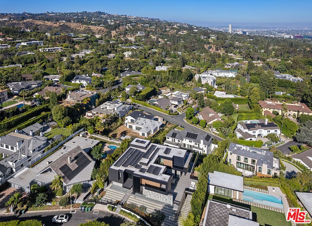 This aerial shot showcases a luxurious residential area with modern homes nestled among lush greenery. The houses feature contemporary architectural designs, some with solar panels, and several properties include swimming pools. The overall impression is one of affluence and serene living within a well-maintained, upscale neighborhood.