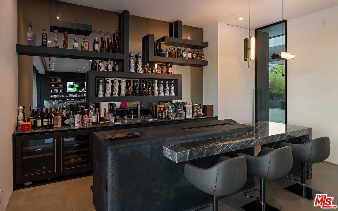 This image showcases a modern wine cellar and bar area, featuring dark cabinetry, open shelving displaying various bottles, and a sleek countertop with bar seating. The design incorporates a sophisticated lighting scheme and a contemporary aesthetic, creating an inviting space for entertaining and wine storage. The perspective is from a medium shot, highlighting the bar area and the seating.