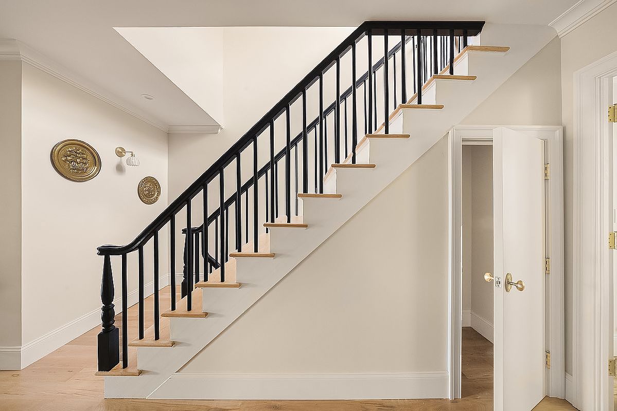 This interior shot showcases a staircase with black railings and wooden steps, set against a neutral-toned wall. The hallway features decorative gold plates and sconces, adding a touch of elegance. A partially open white door hints at another room, creating a sense of depth and flow within the home.