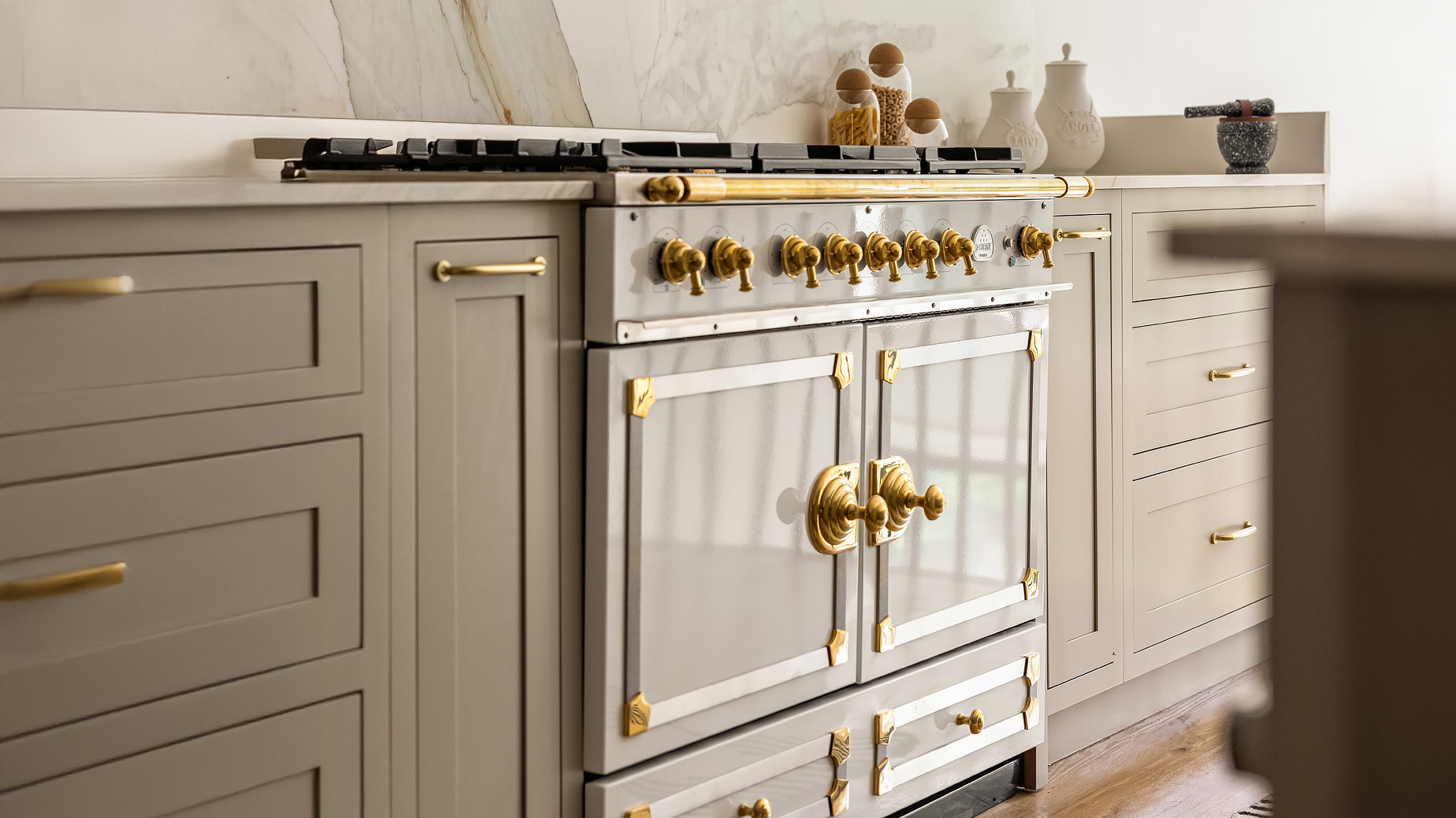 This image showcases a beautifully appointed kitchen featuring custom cabinetry with elegant gold hardware. A high-end range with matching gold accents serves as a focal point. The countertops appear to be a light stone, complementing the soft grey cabinetry, and creating a sophisticated and upscale culinary space.