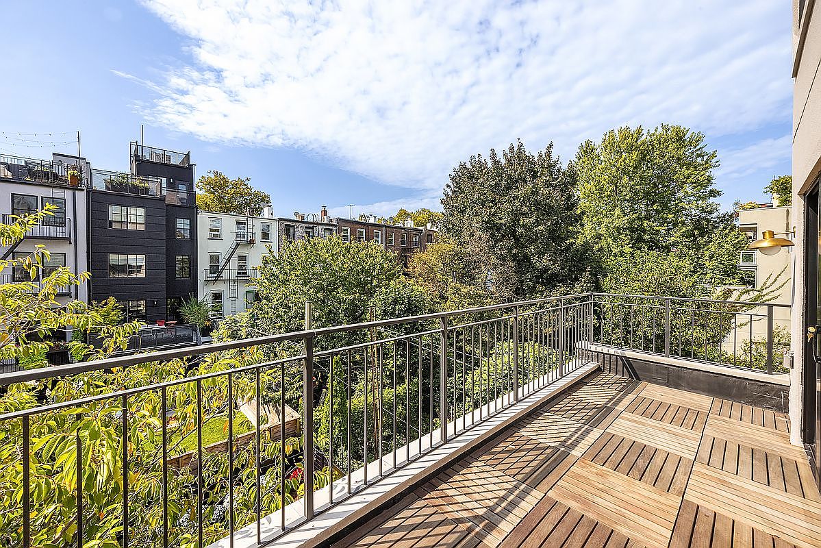 This image showcases a spacious balcony with a wooden deck and metal railing, offering an inviting outdoor living space. The view overlooks lush greenery and neighboring buildings, creating a serene urban oasis. The balcony's design complements the building's architecture, enhancing its appeal.