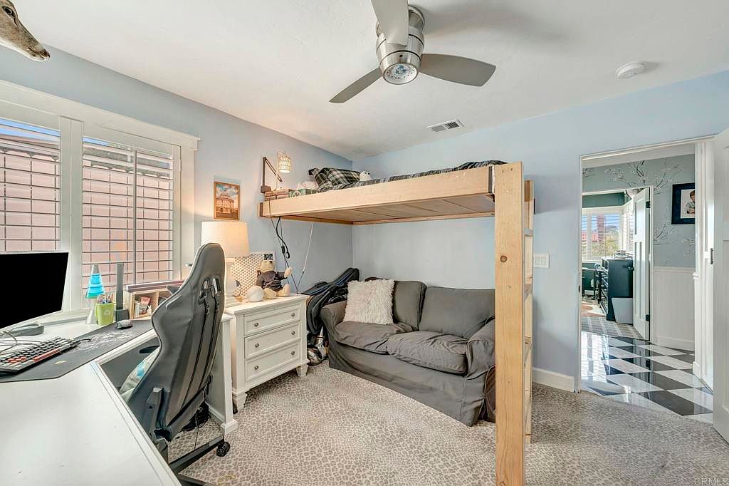 This is a cozy bedroom featuring a unique loft bed design with a couch underneath, maximizing space. The room is painted in a light blue hue, complemented by a white desk and dresser. Natural light streams in through the window, creating a bright and inviting atmosphere.