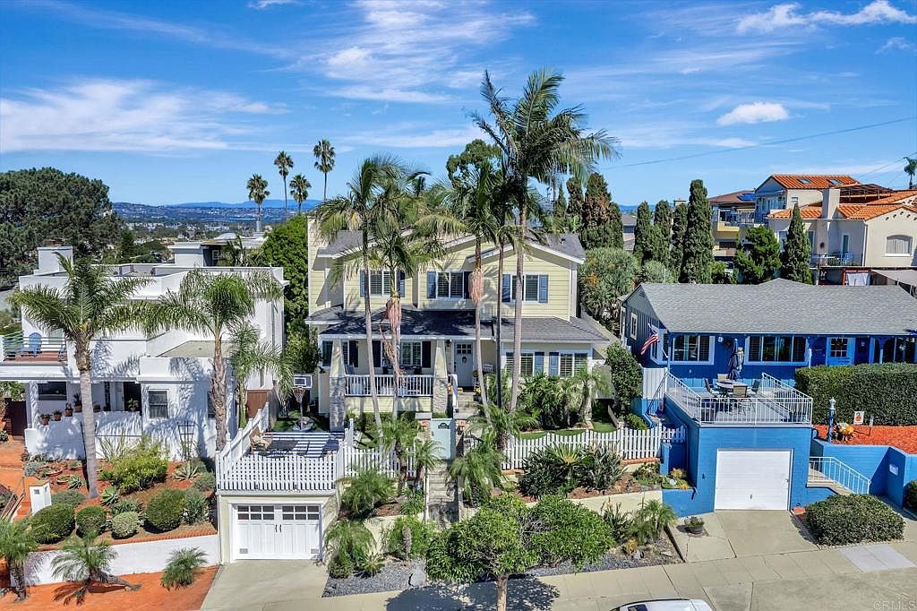 This aerial view showcases three distinct homes, each with unique architectural styles and landscaping. The central yellow house is framed by palm trees, while the white house to the left features a modern design with a rooftop deck. The blue house on the right has a raised deck and a vibrant blue exterior, creating a visually appealing composition.