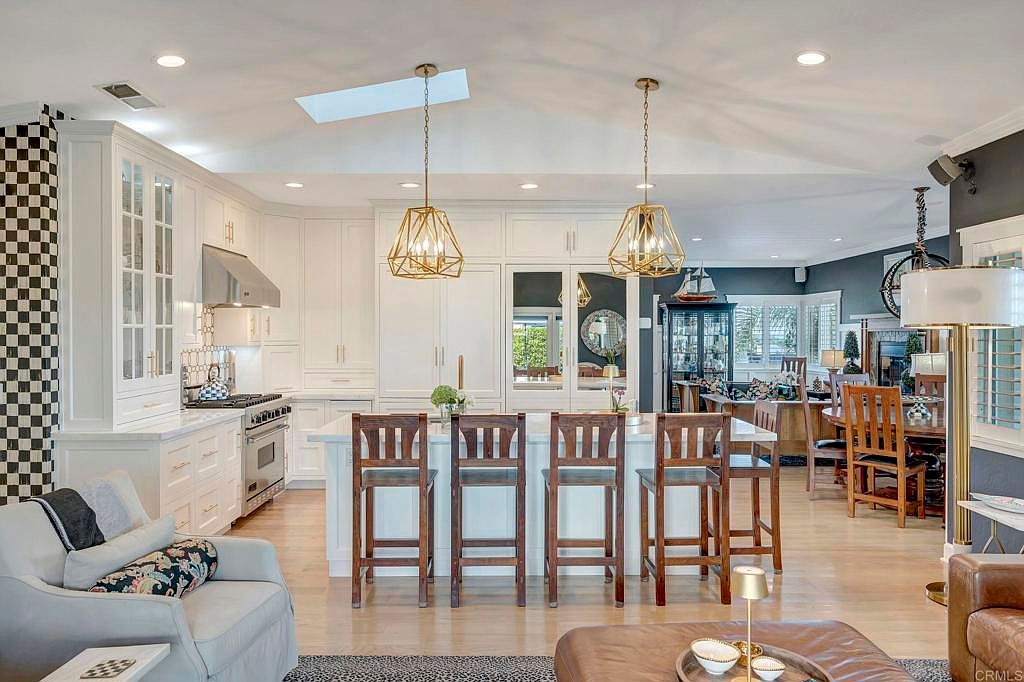 This is a bright and airy kitchen featuring white cabinetry, a large central island with seating, and modern pendant lighting. The open-concept design seamlessly connects the kitchen to the living area, creating a spacious and inviting atmosphere. The checkerboard wall adds a unique design element.