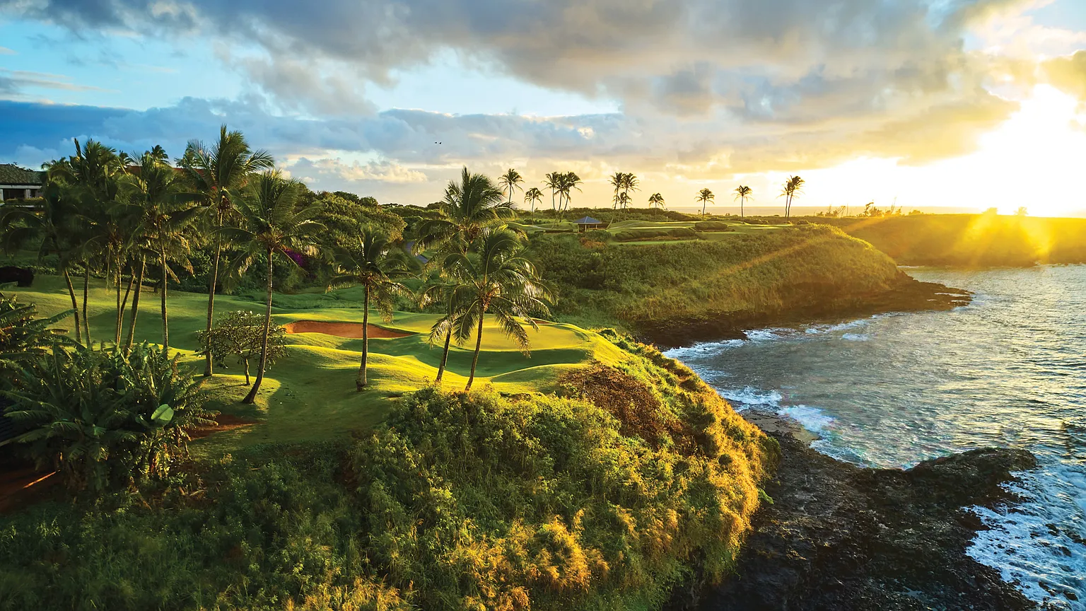 This aerial view captures a stunning golf course situated along a coastline. Lush green fairways and palm trees contrast beautifully with the rocky cliffs and the ocean. The image conveys a sense of luxury, recreation, and potentially, the prestigious location of a high-end property.