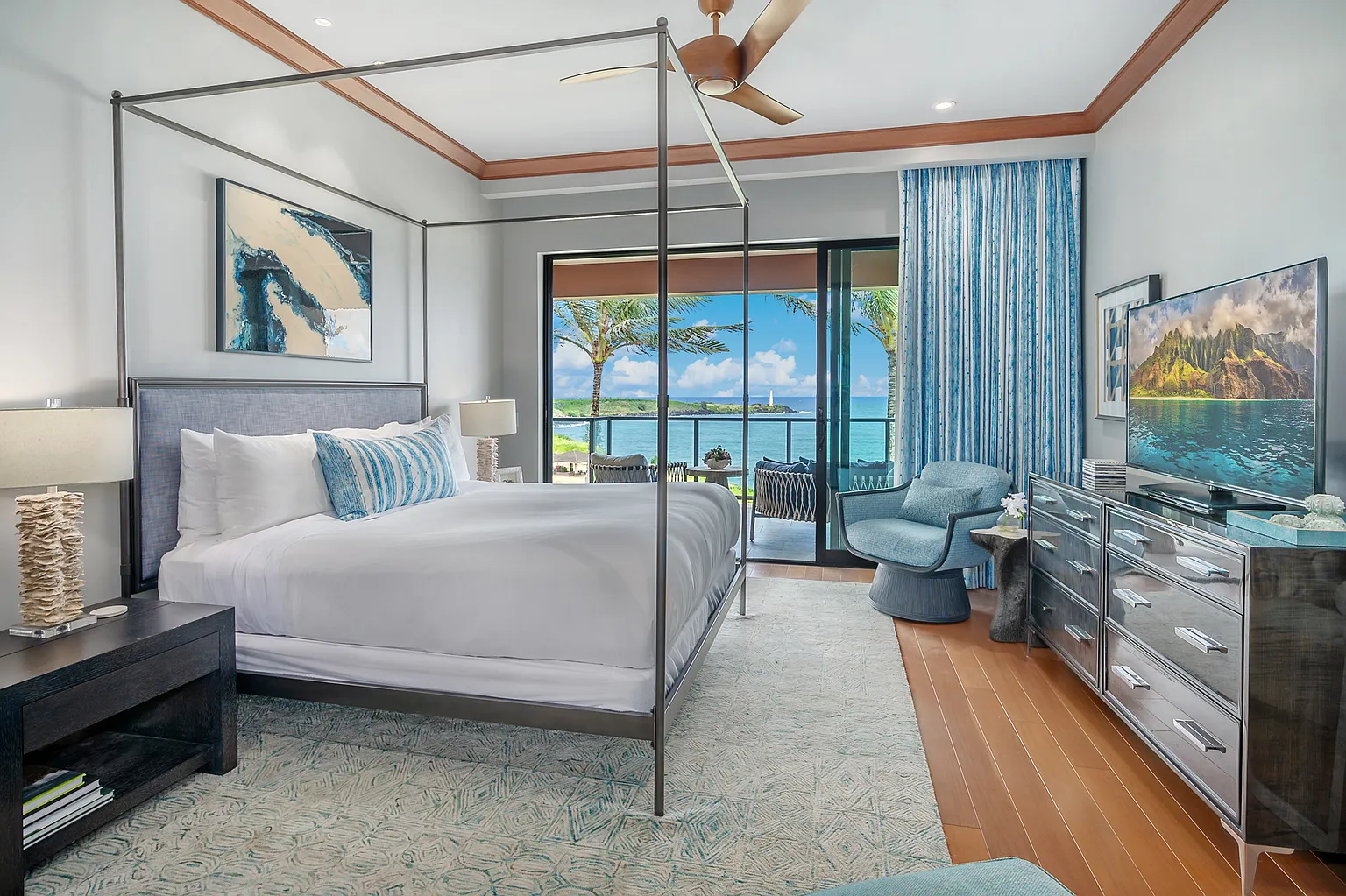 This is a beautifully designed primary bedroom with a four-poster bed, offering a luxurious and relaxing atmosphere. The room features a balcony with ocean views, adding to the appeal. The décor is elegant with a soothing color palette, complemented by well-chosen furnishings, creating a serene and inviting space.
