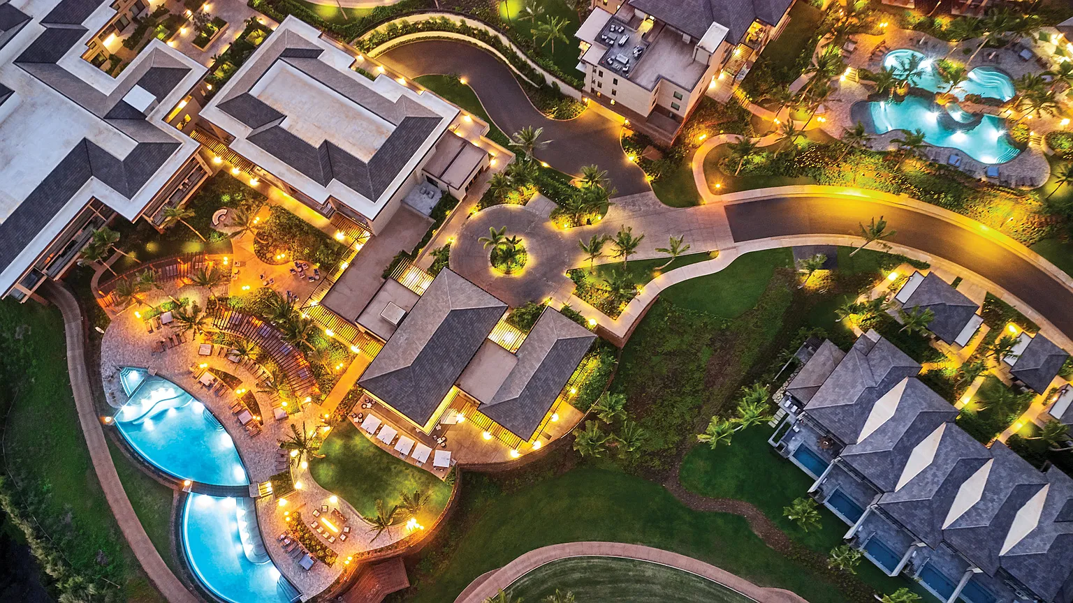This is an aerial view showcasing a luxury resort or residential community. The image highlights multiple pools, manicured landscaping, and elegantly designed buildings with well-lit pathways. The overall impression is one of high-end living and leisure with a focus on outdoor amenities and sophisticated design.