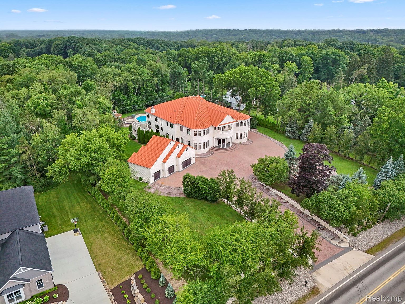 This aerial view showcases a grand estate with a red tile roof, white exterior, and meticulously landscaped grounds. A circular driveway leads to the main entrance, while a separate structure houses a garage. A swimming pool is nestled among the lush greenery, creating a private oasis.