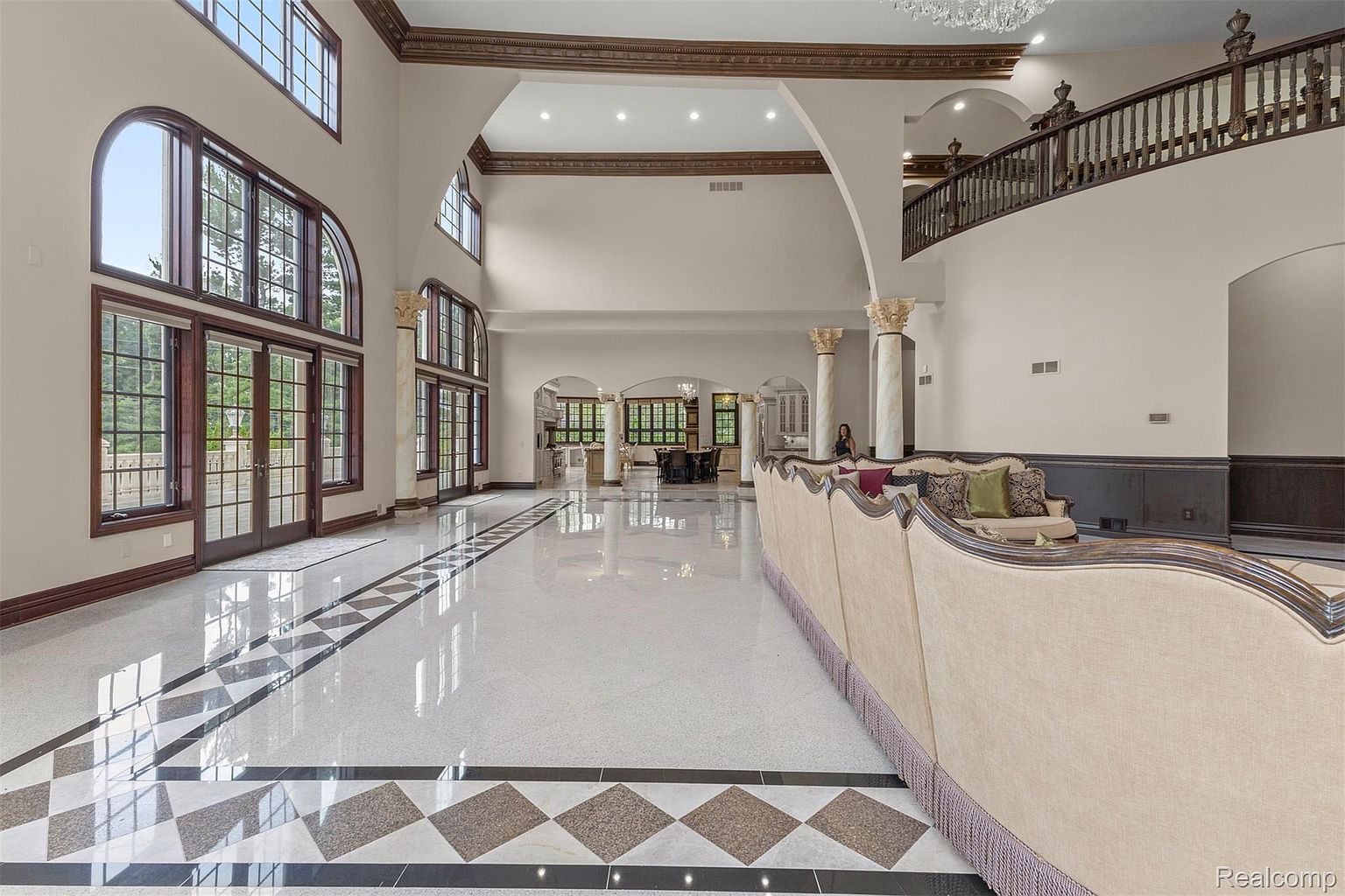 This grand living room features soaring ceilings, large windows, and a striking black and white patterned floor. A long, elegant sofa anchors the space, while architectural columns add a touch of classical sophistication. The room exudes luxury and spaciousness, perfect for entertaining or relaxing.