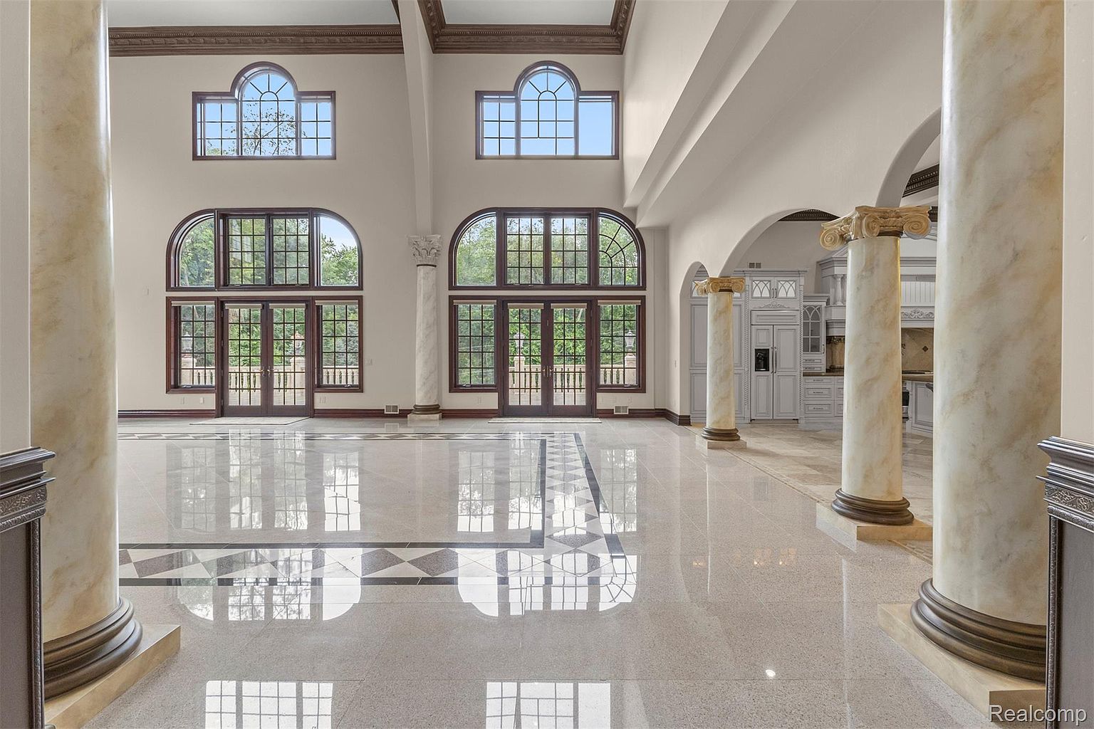 This grand living room features soaring ceilings, large arched windows, and elegant marble columns. The polished marble floors reflect the natural light, creating a bright and airy atmosphere. The room's design exudes luxury and sophistication, making it an impressive space for entertaining or relaxing.