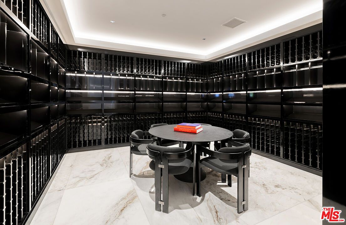 This is a modern wine cellar featuring a black shelving system designed to hold numerous bottles. A round table with chairs sits in the center of the room, suggesting a tasting area. The marble flooring adds a touch of elegance, and the overall design is sleek and sophisticated.