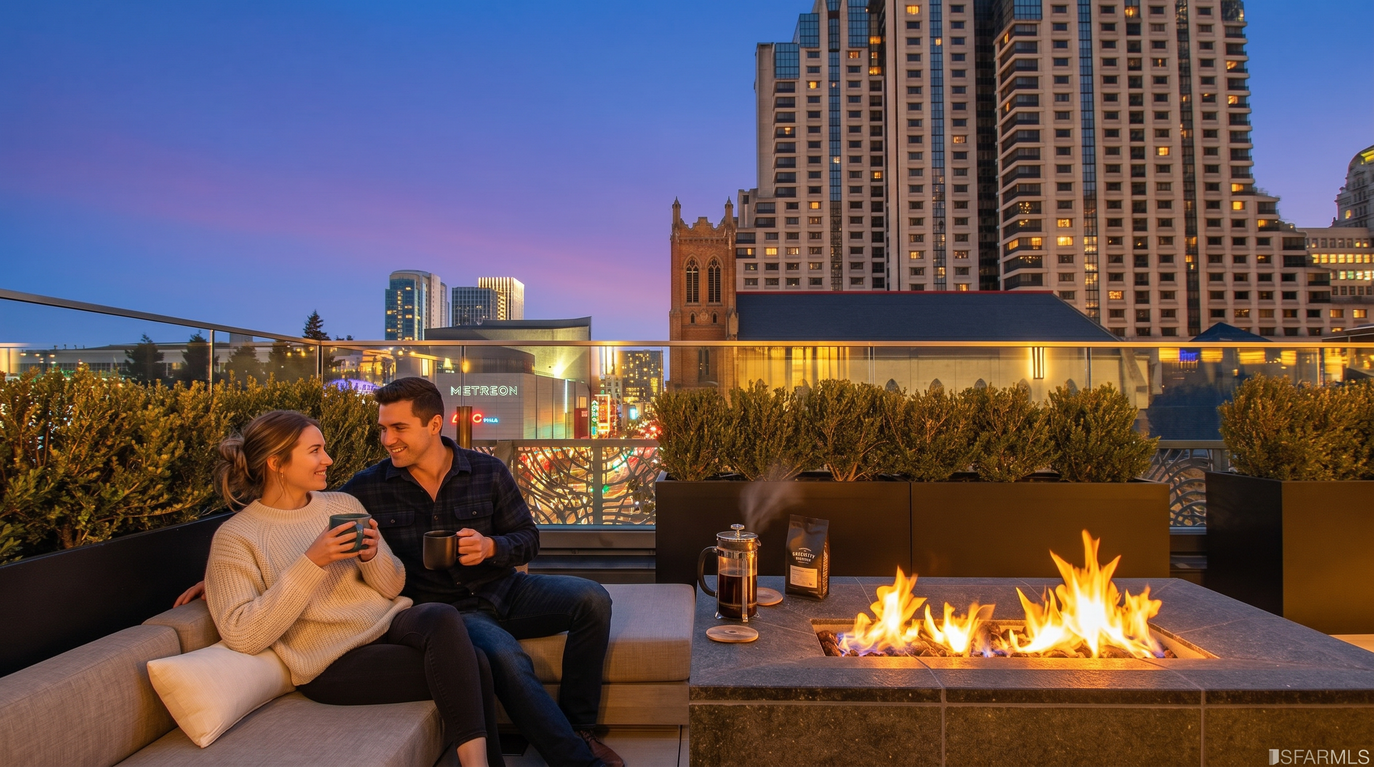 This scenic rooftop balcony offers an exceptional urban setting, featuring a modern built-in stone fire pit and comfortable lounge seating perfect for relaxation. The space is complemented by manicured shrubbery and a glass railing, providing stunning, unobstructed panoramic views of the city skyline at dusk. The warm, inviting atmosphere is enhanced by a coffee setup, making it an ideal amenity space for residents.