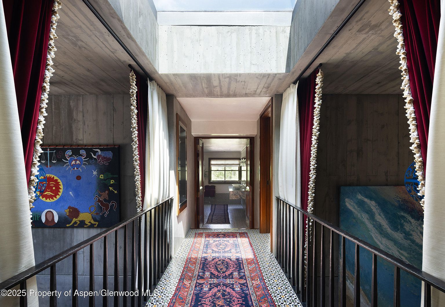 This interior shot showcases a unique hallway with exposed concrete walls and a skylight, creating a modern and industrial aesthetic. The hallway features a patterned rug, artwork on the walls, and curtains, adding warmth and visual interest to the space. A railing lines the hallway, providing safety and a sense of enclosure.