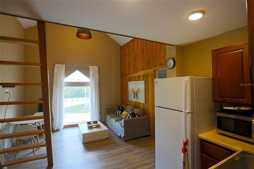 This interior shot showcases a cozy living space with a rustic touch. A wooden ladder leads to an upper level, while a comfortable sofa sits near a window providing natural light. The room features a blend of wood paneling and painted walls, creating a warm and inviting atmosphere.