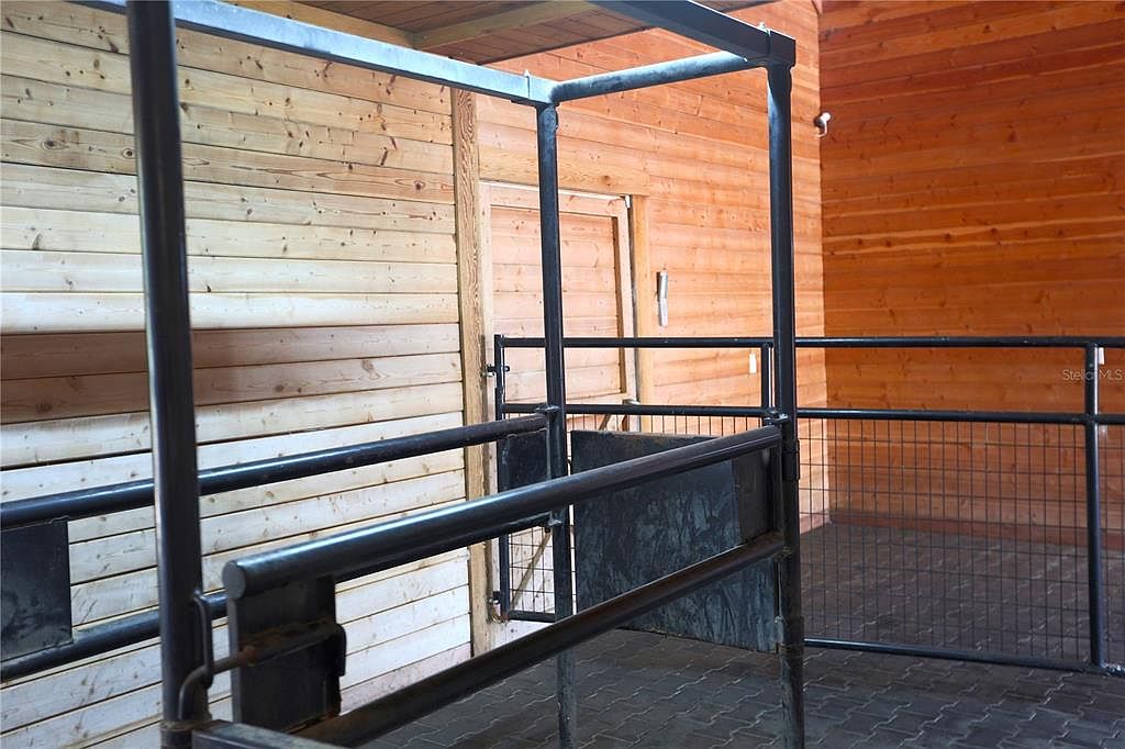 The image showcases the interior of what appears to be a barn or stable, featuring wooden walls and a metal structure, possibly a holding pen or stall. The space is well-lit, highlighting the natural wood grain and the functional design of the metalwork. The overall impression is one of a sturdy and practical agricultural building.
