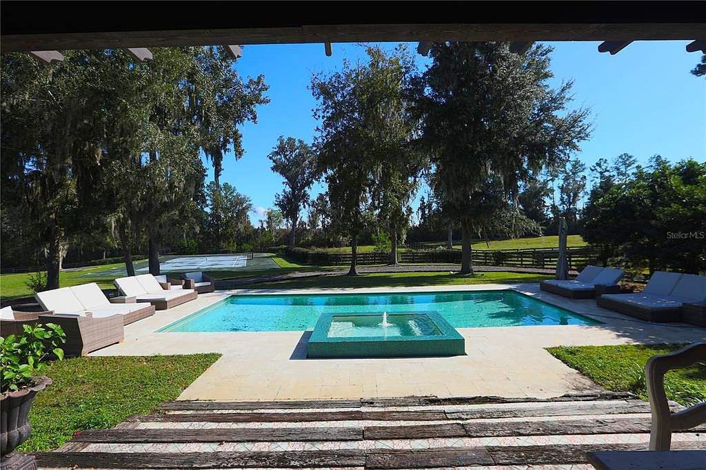 This image showcases a luxurious outdoor pool and spa area. The pool features a modern design with a separate spa section, surrounded by lounge chairs and lush greenery. The setting evokes a sense of relaxation and upscale outdoor living, perfect for entertaining or enjoying a private retreat.