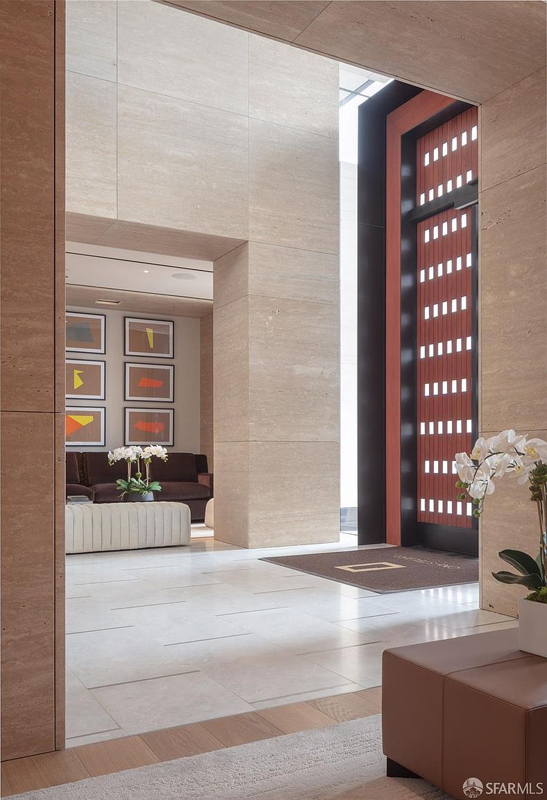 This interior shot showcases a luxurious hallway or lobby area, featuring travertine walls and flooring. The space is well-lit and includes modern artwork, comfortable seating, and elegant floral arrangements. The overall impression is one of sophistication and high-end design, creating an inviting and stylish atmosphere.