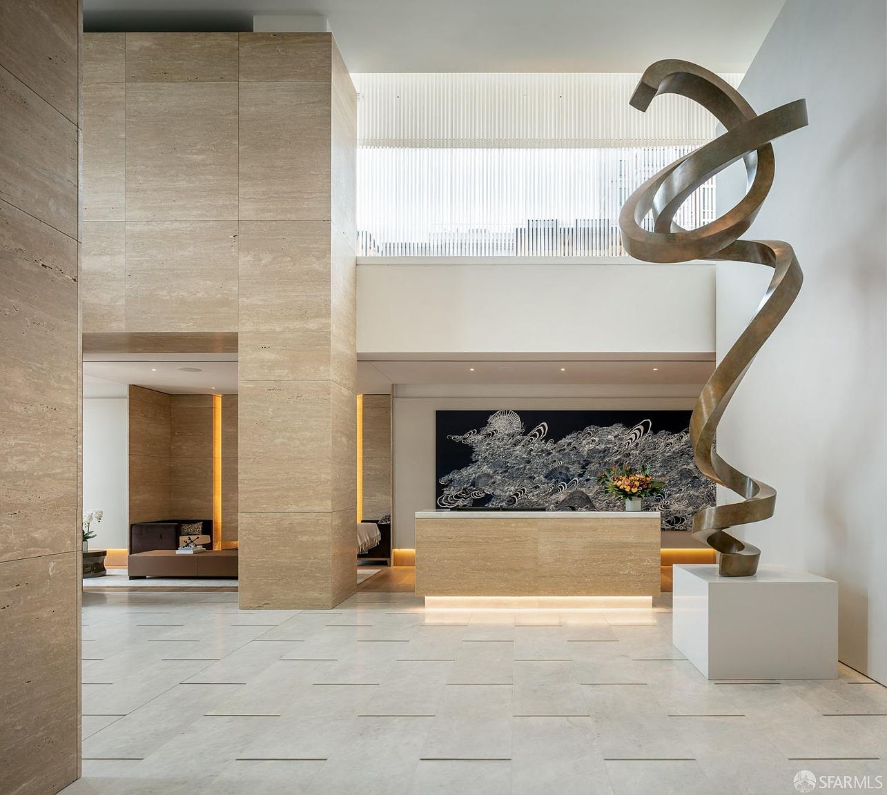 This is an interior shot of a luxurious lobby or hallway, featuring travertine walls and flooring. A large, abstract metal sculpture stands prominently near the reception desk, which is adorned with a black and white abstract painting. The space is well-lit and exudes a modern, sophisticated ambiance, perfect for a high-end residential building or hotel.