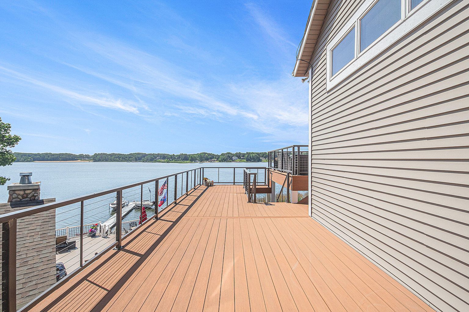 This image showcases a spacious outdoor deck with a modern design, featuring a sleek railing system and a light brown composite decking material. The deck offers stunning views of the water and surrounding landscape, creating an inviting outdoor living space. The exterior of the house is clad in horizontal siding, complementing the deck's contemporary aesthetic.