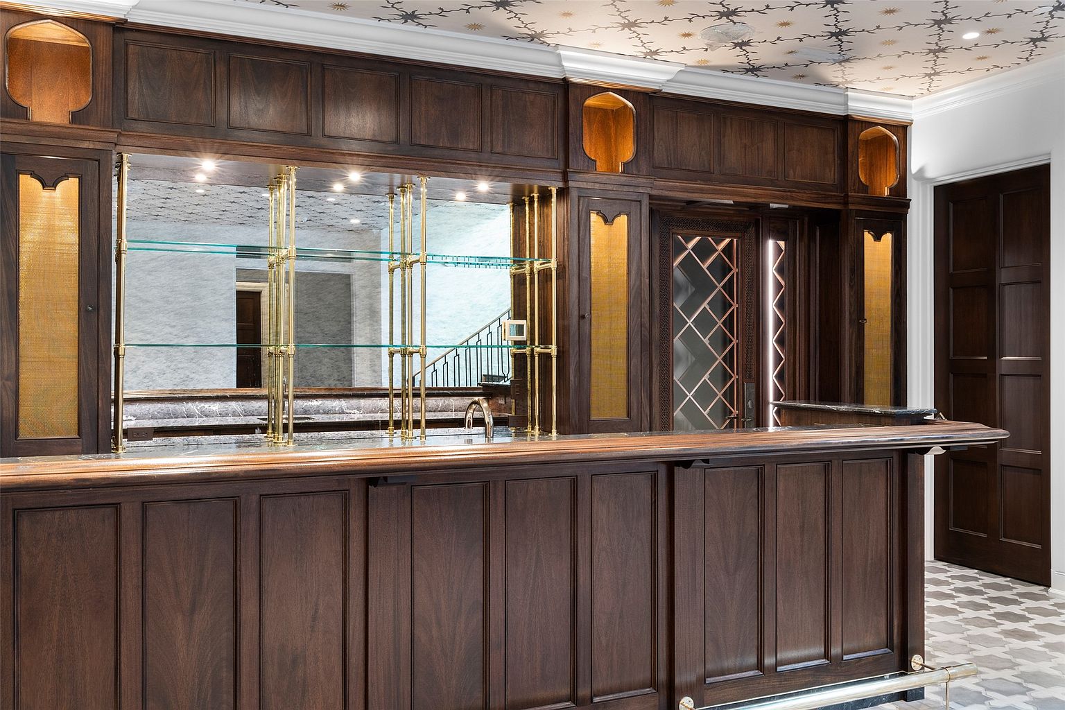 This image showcases a sophisticated wine cellar featuring dark wood cabinetry with glass shelving and mirrored backdrops. The bar area is well-lit, highlighting the rich wood tones and elegant design. The overall impression is one of luxury and refined taste, perfect for showcasing a high-end property.