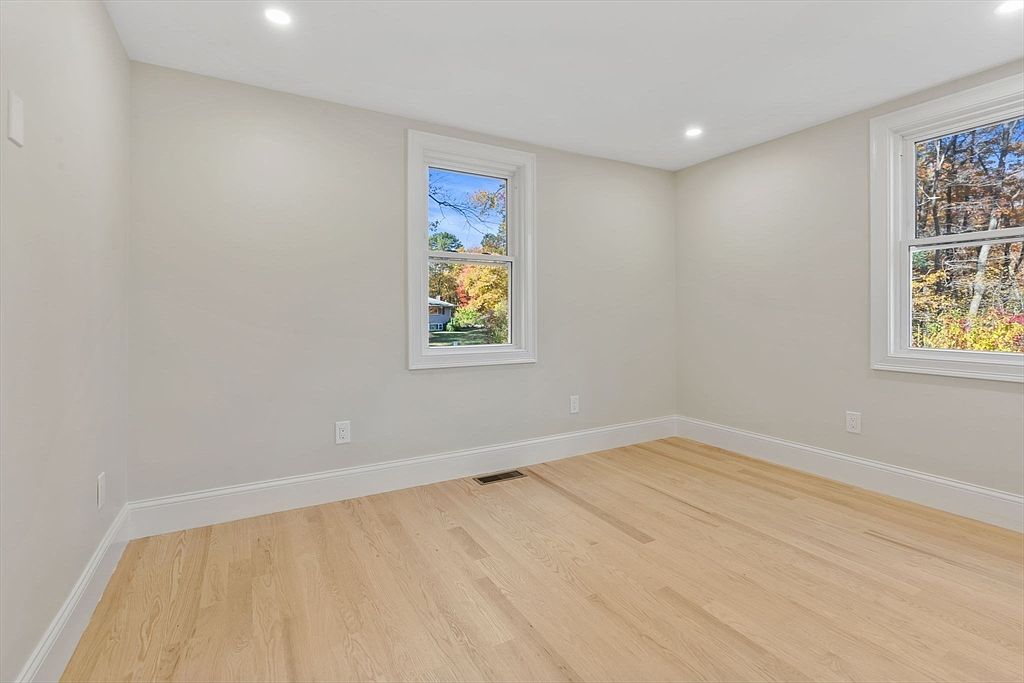 This is a bright, empty bedroom with light hardwood floors and neutral-colored walls. Two windows provide natural light and views of the outdoors. The room is clean and ready for personalization, offering a blank canvas for potential buyers.