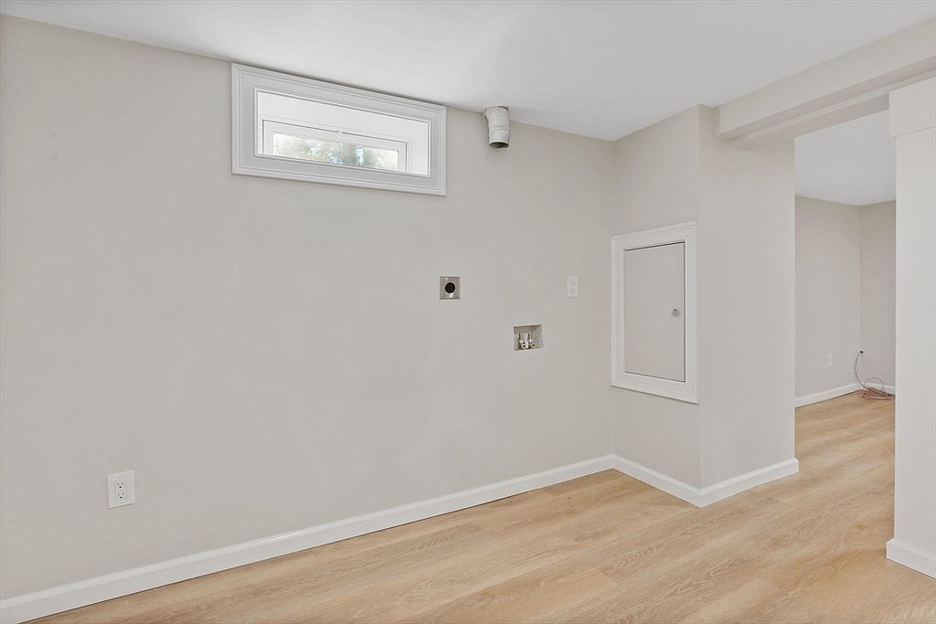 The image showcases a freshly renovated basement space, featuring light wood-look flooring and neutral-toned walls. A small window provides natural light, while utility connections suggest laundry capabilities. The room's clean lines and minimalist design create a versatile and inviting atmosphere, perfect for a potential buyer seeking a functional and modern space.