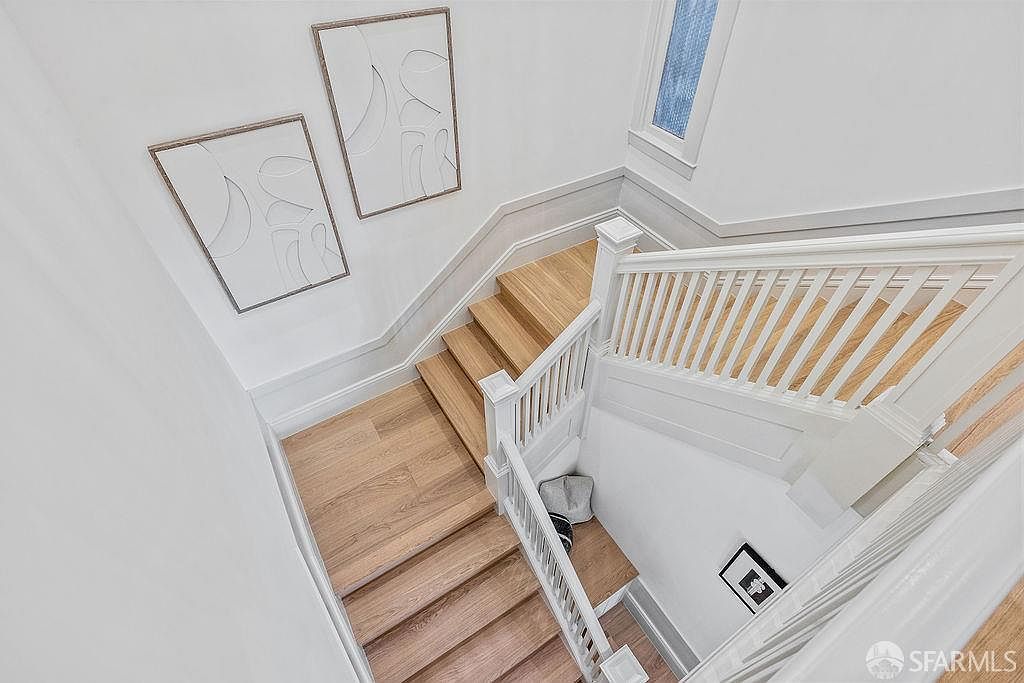 This is a high-angle shot of a staircase featuring light wood steps and white railings. Two framed pieces of art hang on the wall alongside the stairs, adding a touch of modern elegance. The overall impression is clean, bright, and well-maintained, suggesting a sophisticated and inviting home.