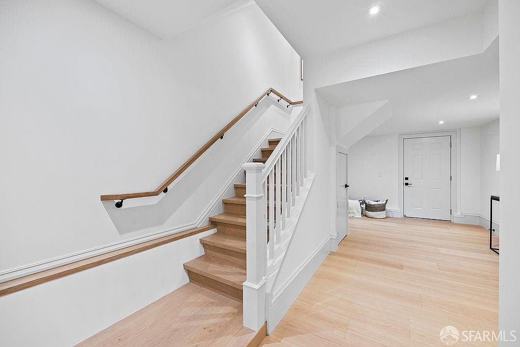 This interior shot showcases a bright hallway with wooden stairs and white walls, creating a clean and modern aesthetic. The wooden handrail and light wood flooring add warmth to the space, while the white door at the end of the hallway suggests access to another room. The overall impression is one of simple elegance and functionality.