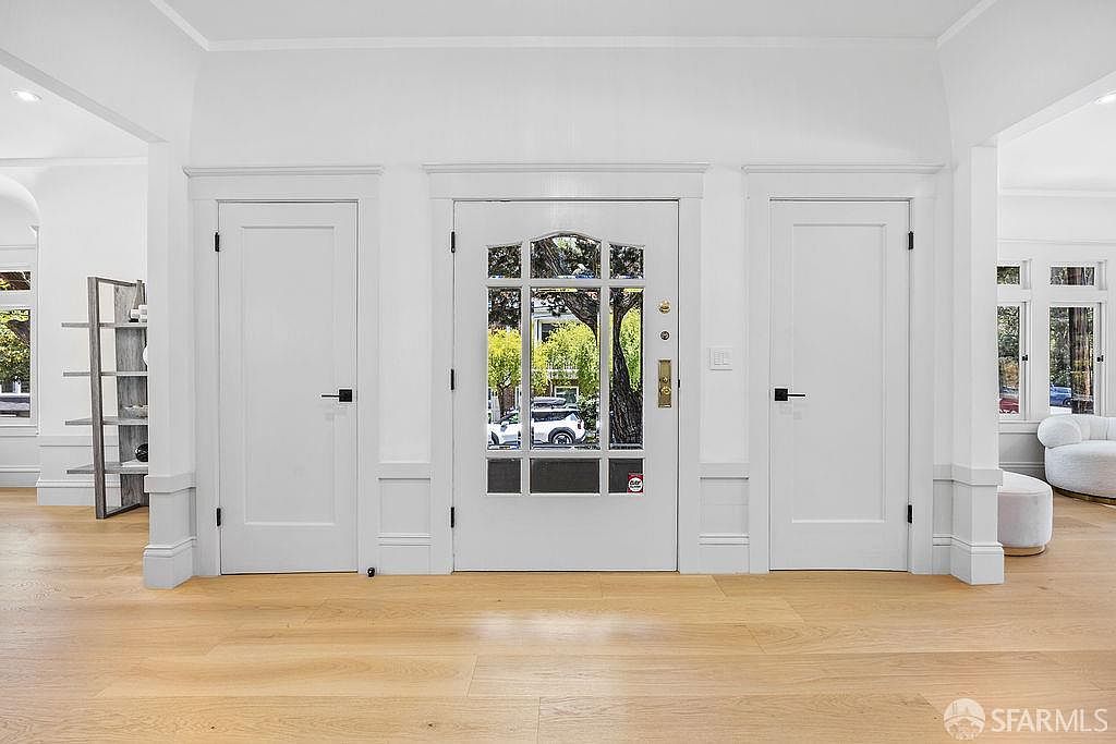 This interior shot showcases a bright and inviting hallway with light wood flooring and white walls. Three white doors are prominently featured, with the central door having a glass panel offering a glimpse of the exterior. The space is well-lit and appears clean and modern, creating a welcoming entrance to the home.