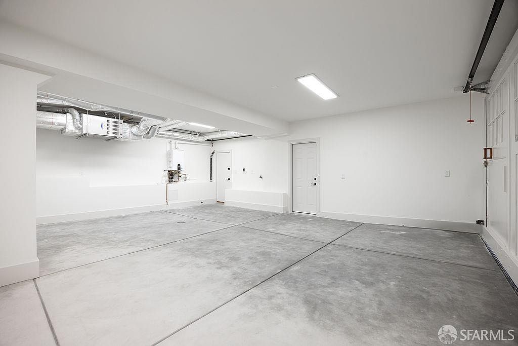 This is an interior shot of a spacious, modern garage. The concrete floor is divided into large sections, and the walls and ceiling are painted white. The garage features a water heater, ductwork, and two doors, creating a clean and functional space.