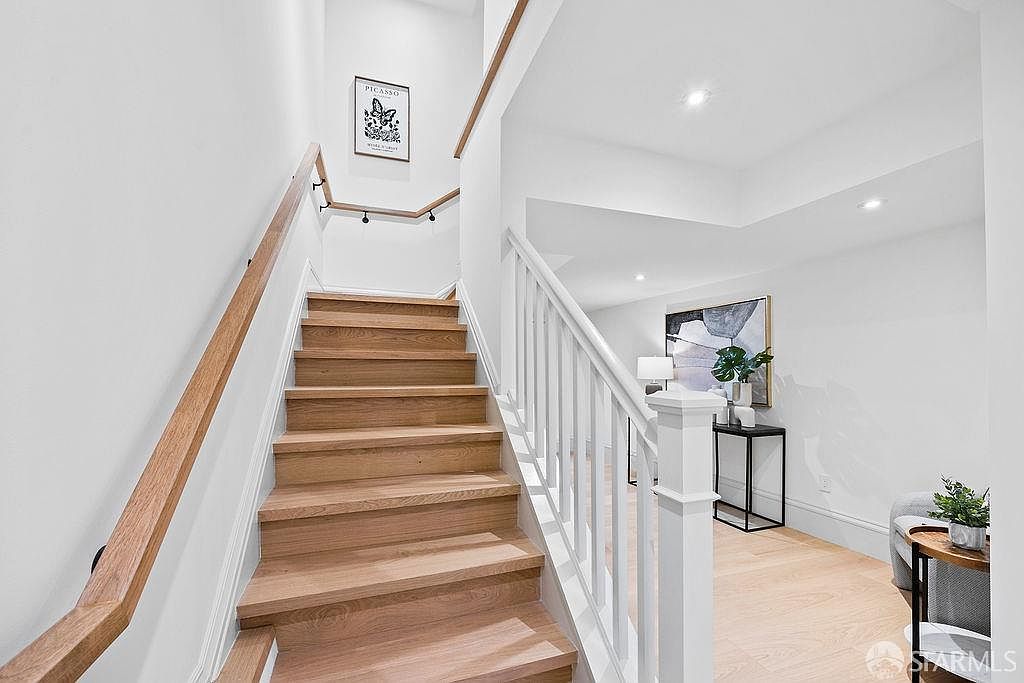 This interior shot showcases a well-lit hallway with wooden stairs and white railings. A framed Picasso print adorns the wall above the stairs, adding a touch of sophistication. The space is bright and clean, creating an inviting transition between levels of the home.