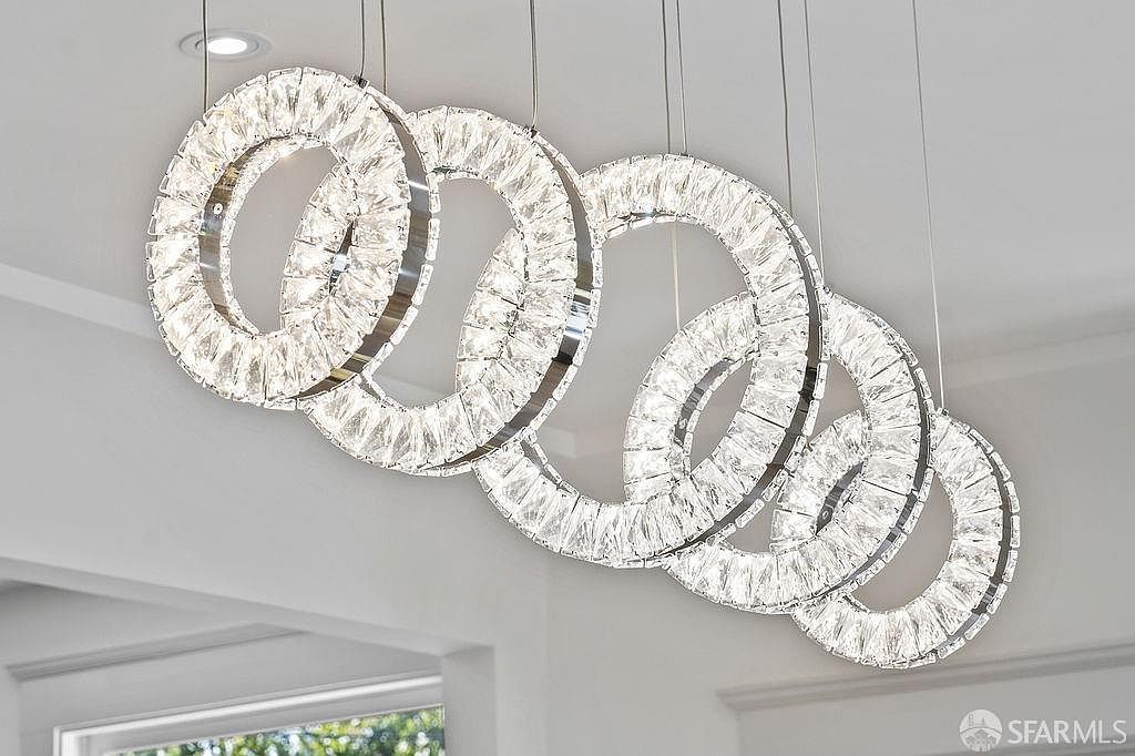 The image showcases a modern chandelier composed of multiple interconnected crystal-studded rings, suspended from the ceiling. The fixture's design creates a visually striking and luxurious focal point, enhancing the ambiance of the space with its reflective surfaces and intricate detailing. The lighting fixture adds a touch of elegance and sophistication to the interior.