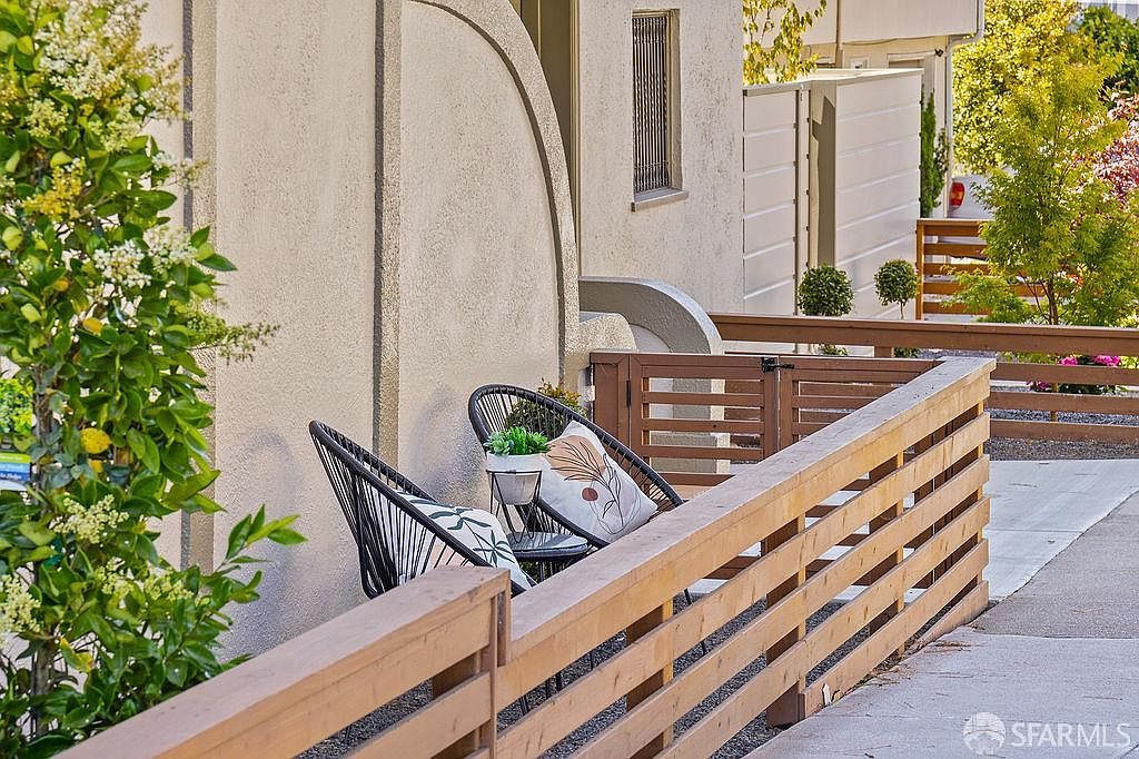 This image showcases an inviting outdoor patio area. Two black wicker chairs with patterned cushions are arranged around a small table, creating a cozy seating arrangement. A wooden fence encloses the space, and lush greenery adds a touch of nature, enhancing the overall appeal of this outdoor living space.