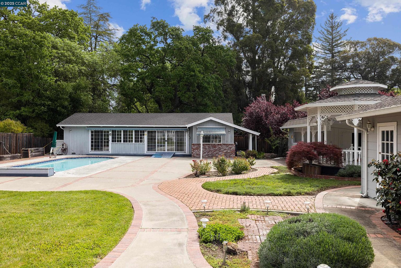 This image showcases a beautifully landscaped backyard featuring a pool, a charming gazebo, and meticulously maintained gardens. A winding brick pathway connects the various elements, creating an inviting and serene outdoor space. The property exudes a sense of tranquility and privacy, making it an ideal setting for relaxation and entertainment.