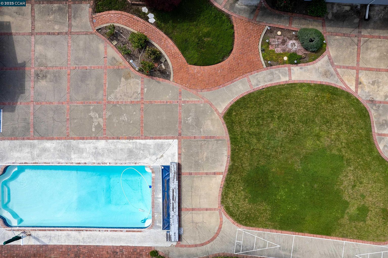 This aerial shot showcases a well-maintained backyard featuring a rectangular swimming pool with clear blue water, surrounded by a concrete patio with brick accents. Lush green lawns and meticulously designed garden beds add to the property's appeal. The overall impression is one of a private and inviting outdoor space perfect for relaxation and entertainment.