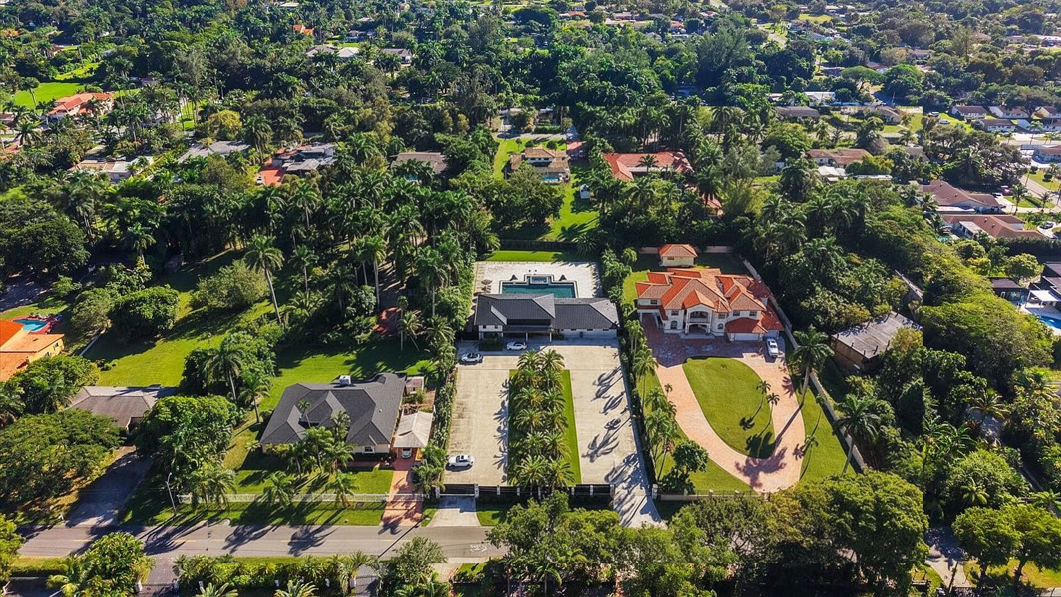 This is an aerial view showcasing multiple luxury homes surrounded by lush greenery and mature trees. The properties feature well-manicured lawns, private driveways, and swimming pools. The image emphasizes the spaciousness and exclusive setting of the real estate.